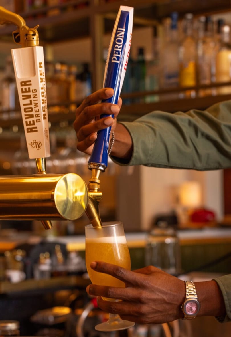 Bartender pouring a golden beer from a Peroni tap into a glass at a bar.